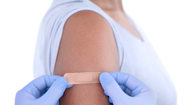 Ärztin klebt nach einer Impfung ein Pflaster auf den Arm einer Patientin | Bild: mauritius images / Science Photo Library