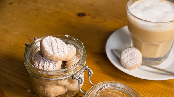 Ein Glas mit frischen Heidesand-Keksen steht neben einem Glas mit Milchkaffee. | Bild: BR/ Kathrin Martin
