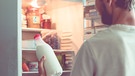 Mann hält Milchflasche vor Kühlschrank | Bild: mauritius images  Mikhail Rudenko  Alamy  Alamy Stock Photos