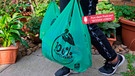 Eine Frau trägt zwei Plastiktüten mit der Aufschrift "100 Prozent kompostierbar" | Bild: mauritius images