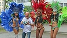 WM-Song: Bayern 1-Moderator Stephan Lehmann hält einen Fußball und wird von drei bunt geschmückten brasilianischen Tänzerinnen umringt | Bild: BR/Veronika Holzer