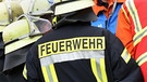 Feuerwehrmann trägt Jacke mit der Aufschrift "Feuerwehr" auf dem Rücken | Bild: picture-alliance/dpa