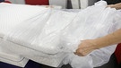 Eine Frau zieht eine neue Matratze aus einer Plastikfolie. | Bild: picture-alliance/dpa