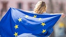 Eine junge Frau hält eine Europaflagge. | Bild: stock.adobe.com/weyo