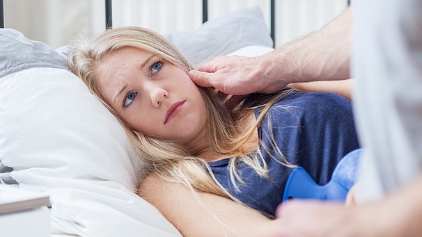 Frau im Bett mit kränklichem Blick, lässt sich von ihrem Partner trösten. | Bild: picture-alliance/dpa
