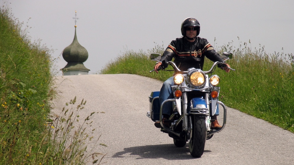 Ein Mann fährt eine Harley Davidson, im Hintergrund eine Kirchturmspitze | Bild: picture-alliance/dpa