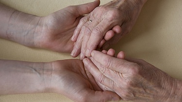 Hände einer Pflegerin halten die Hände einer zu pflegenden Person. | Bild: BR / Natasha Heuser