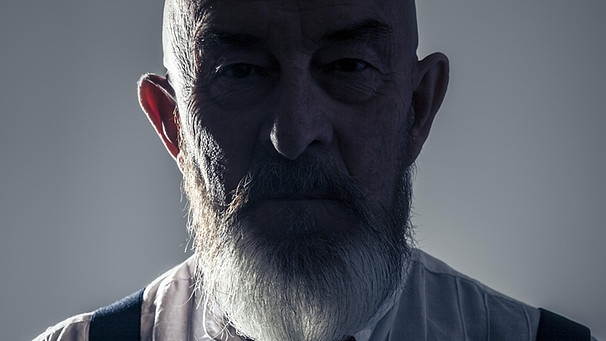 Älterer Mann mit Bart, der düster dreinschaut und dessen Gesicht im Schatten liegt. | Bild: picture-alliance/dpa