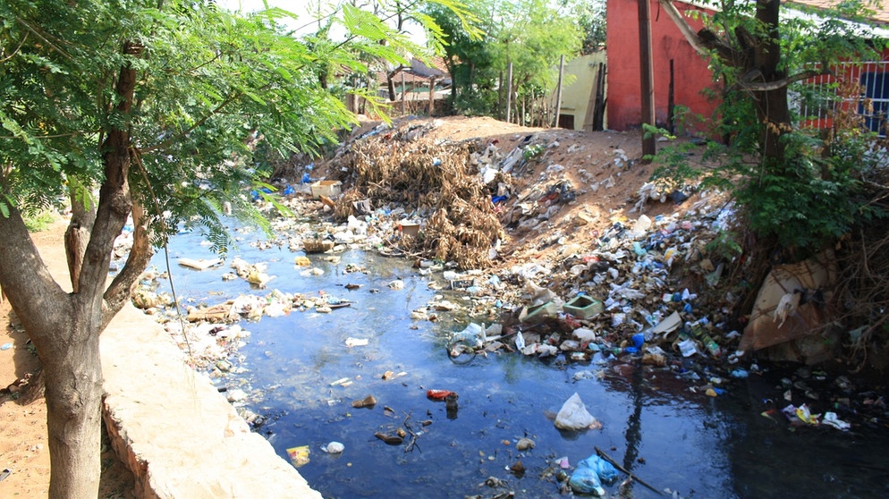 Ein kleiner Fluss neben eine Holzbaracke, der voller Müll ist, auch das Ufer ist übersät mit Abfall | Bild: picture-alliance/dpa