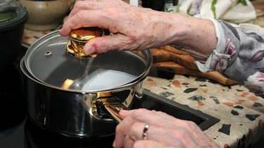 Ältere Frau hält einen Kochtopf auf dem Herd | Bild: picture-alliance/dpa