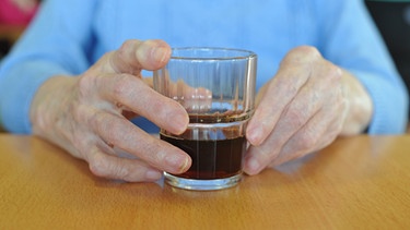 Älterer Mensch sitzt vor einem Getränk und hält es fest | Bild: picture-alliance/dpa