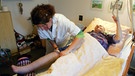 Thrombosen treten insbesondere bei Bewegungsarmut auf - im Bild: Altenpflegerin bei der Fixierung eines Stützstrumpfes einer Patientin | Bild: picture-alliance/dpa