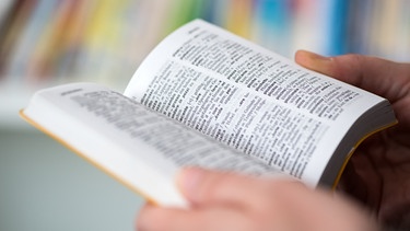 Eine Person hält ein Wörterbuch in der Hand. | Bild: picture alliance/dpa Themendienst/Andrea Warnecke