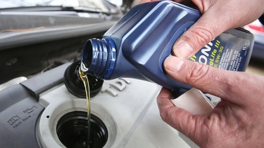 Ein Mann füllt  Motoröl in den Motor seines Fahrzeugs ein | Bild: picture-alliance/dpa