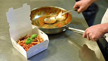 In einer Küche wird eine frisch gekochte Bestellung in einen Behälter gefüllt und für die Auslieferung fertig gemacht. | Bild: picture-alliance/dpa