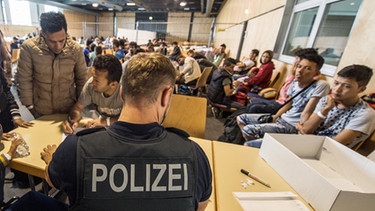 Ein Beamter der Bundespolizei nimmt im Notquartier der Bundespolizeiinspektion in Passau Namen von Flüchtlingen auf. | Bild: picture-alliance/dpa