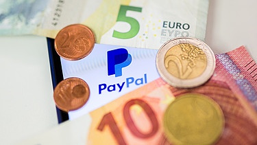 Symbolbild: Münzen und Geldscheine vor einem Paypal-Symbol | Bild: picture-alliance/dpa