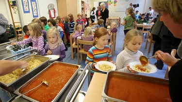 Schulverpflegung: Schülerinnen bekommen ein Mittagessen auf die Teller portioniert | Bild: picture-alliance/dpa