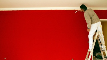 Ein Maler streicht eine Wand rot an | Bild: picture-alliance/dpa