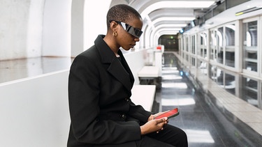 Young woman wearing smart glasses and using smart phone at metro station | Bild: picture alliance / Westend61 | NOVELLIMAGE