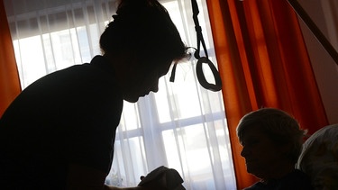 Eine alte Frau wird von einer Pflegerin umgebettet | Bild: picture-alliance/dpa