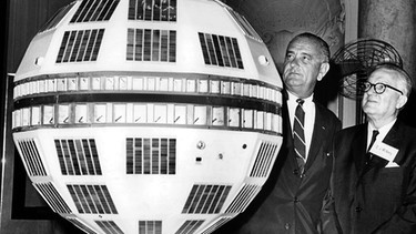 US-Vize-Präsident Lyndon B. Johnson (l) und Eugene J. McNeeley (r), Präsident der US-Telefongesellschaft neben einem Model des Kommunikationssatelliten Telstar  | Bild: picture-alliance/dpa