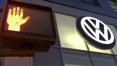 Das Logo von Volkswagen leuchtet am 26.09.2015 an der Fassade der Volkswagen Niederlassung «Manhattan» in New York in den USA. Links leuchtet eine rote Fußgängerampel.  | Bild: picture-alliance/dpa