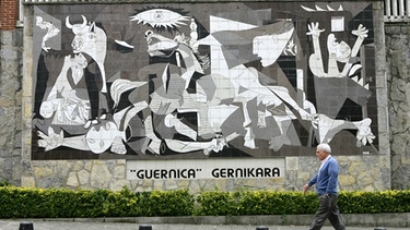 Ein Mann geht an dem als Mosaik reproduzierten Gemälde "Guernica" von Pablo Picasso in Guernica vorbei. Mit seinem wohl bekanntesten Bild erinnerte Picasso an die verheerende Bombardierung des spanischen Städtchens 1937. | Bild: picture-alliance/dpa