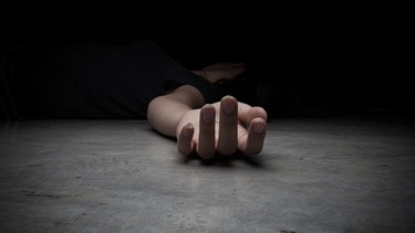 Eine Frau liegt reglos im Dunkeln auf dem Boden. Nur die rechte Hand ist angeleuchtet. | Bild: stock.adobe.com/aradaphotography