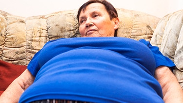 übergewichtige ältere Frau in blauem T-Shirt liegt auf einem Sofa | Bild: colourbox.com