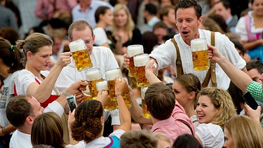 Wiesnbesucher feiern in einem Bierzelt auf dem Oktoberfest in München nach dem Anzapfen mit ihrer ersten Maß (Archivbild). | Bild: picture-alliance/dpa/Sven Hoppe