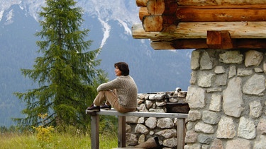 Frau sitzt vor Berghütte | Bild: picture-alliance/dpa