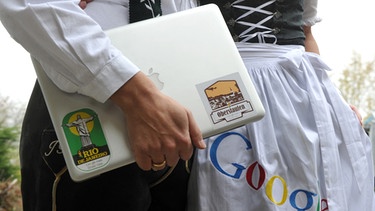 Mit Dirndl, Laptop und Lederhose ist ein Paar ausgestattet, auf der Dirndlschürze befindet sich der Name Google. | Bild: picture-alliance/dpa