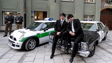 Die beiden Schauspieler Brad Henshaw (als Elwood Blues, 2.v.r) und Jim de Groot (als Jake Blues, r) stehen am 04.02.2010 in München (Oberbayern) vor dem Polizeipräsidium.  | Bild: picture-alliance/dpa