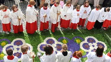 Ministranten warten an Fronleichnam während der Prozession an einem Blumenteppich | Bild: picture-alliance/dpa