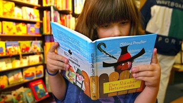 Die 8-jährige Anja Rieder aus Emmenmatt blättert in einer Buchhandlung in Bern im Otfried Preussler-Kinderbuch "Räuber Hotzenplotz". | Bild: picture-alliance/dpa