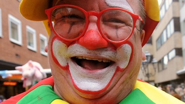 Ein als Clown kostümierter Teilnehmer lacht in Nürnberg beim Faschingsumzug.  | Bild: picture-alliance/dpa