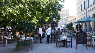 Zwei Kellner warten auf Kundschaft im italienischen Restaurant Tambosi im Hofgarten in München. | Bild: picture-alliance/dpa