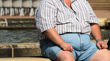 Ein Mann mit Übergewicht sitzt an einem Brunnenrand | Bild: picture-alliance/dpa