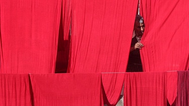 Ein Mann hat große rote Textilbahnen zum Trocknen aufgehängt und prüft sie. | Bild: dpa/Rana Irfan Ali