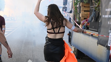 Eine Frau tanzt auf der Straße. Sie geht neben einem Wagen her und hebt den linken Arm in die Luft.  | Bild: picture alliance / SZ Photo | Stephan Rumpf