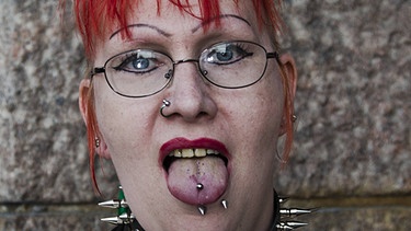 Eine Frau mit Piercings in Zunge und Nase. | Bild: picture-alliance/dpa
