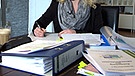 Symbolbild: Frau am Schreibtisch mit mehreren Aktenordnern. | Bild: BR