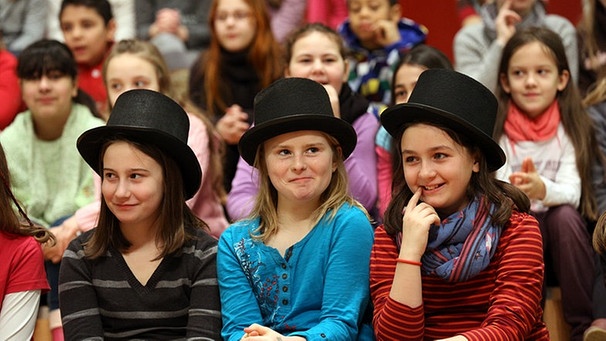 Kinder im Publikum. In der ersten Reihe sitzen drei Mädchen mit schwarzen Zylindern auf dem Kopf. | Bild: ARD