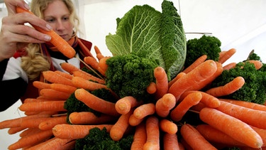 Eine junge Frau steckt eine Karotte in einen Strauß mit Karotten, Grünkohl und Wirsing | Bild: picture-alliance/dpa