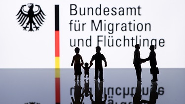 Symbolbild für Flüchtlingshilfe: Logo des Bundesamtes für Migration und Flüchtlinge, davor Figuren, die Helfer symbolisieren | Bild: picture-alliance/dpa