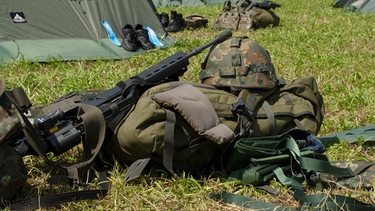  Das Sturmgepäck eines Soldaten liegt auf der Wiese bei einem Zeltlager. | Bild: BR