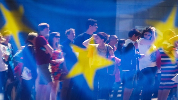 Durch eine EU-Flagge sind Menschen zu sehen | Bild: picture-alliance/dpa