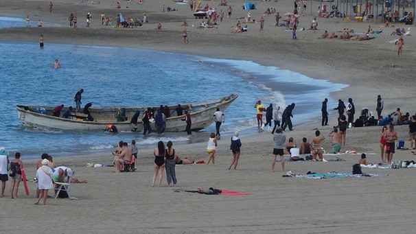 Flüchtlinge landen im Dezember 2020 in einem offenen Boot am Strand von Los Cristianos auf Teneriffa zwischen sich sonnenden Touristen. | Bild: picture alliance/dpa | Andreas Jütte
