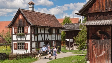 Eine Familie spaziert durch das Bauernhofmuseum am Woringer Häusle vorbei | Bild: Schwäbisches Bauernhofmuseum Illerbeuren